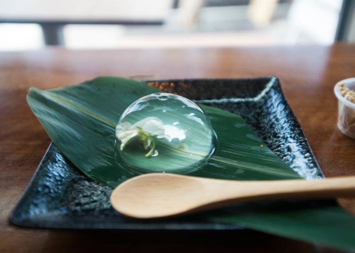 Beautiful Japanese raindrop cake plated on a leaf, with a flower encased in a sweet and refreshing orb of gelatin dessert