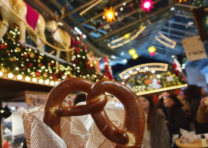 A pretzel being held up with a background of the Christmas market lights