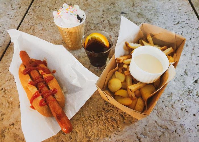 A German-style curry hot dog with ketchup, a box of fries with a cheese dipping sauce and a mulled wine and hot chocolate