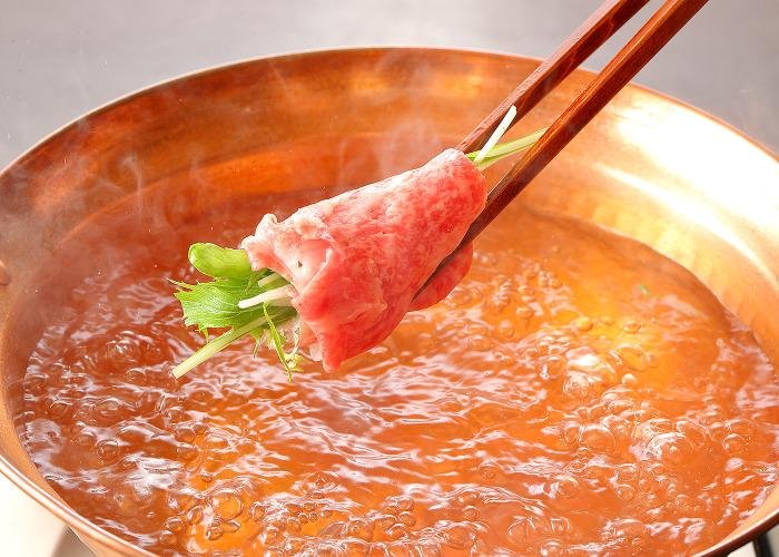 A pot of hot bubbling soup, and chopsticks holding meat ready to be dipped