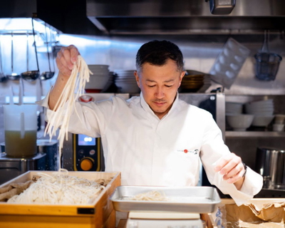 Chef prepares fresh udon noodles in a bustling kitchen