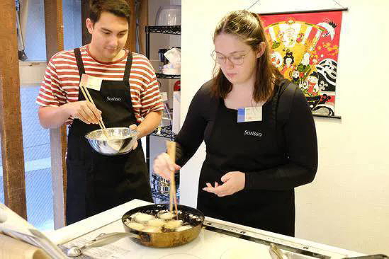 Two people engaged in a Japanese cooking class, frying ingredients together.