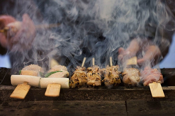 Grilled skewers on smoky barbecue in a bustling restaurant setting