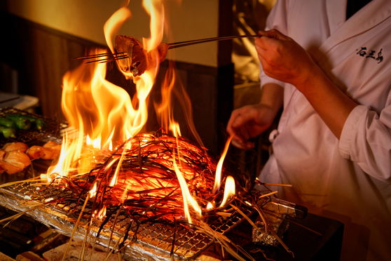 Chef grilling yakitori over open flame at gourmet restaurant