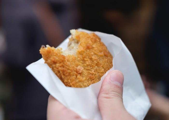 A hand holding a Japanese seafood croquette made with mashed potato and chopped seafood