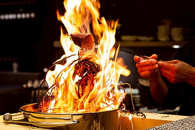 Chef grilling meat over open flame in modern kitchen