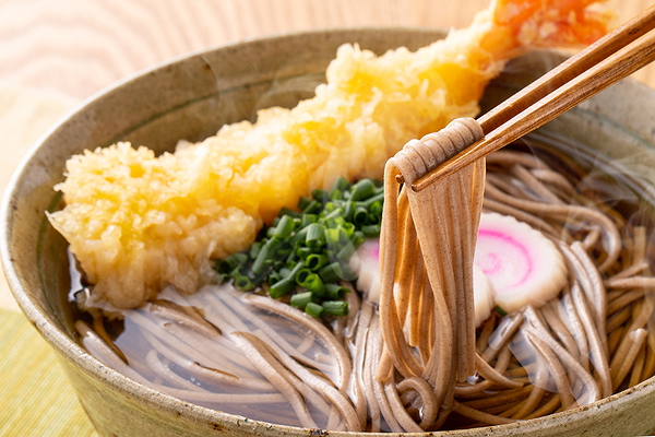 Chopsticks holding soba noodles with tempura and green onion garnish