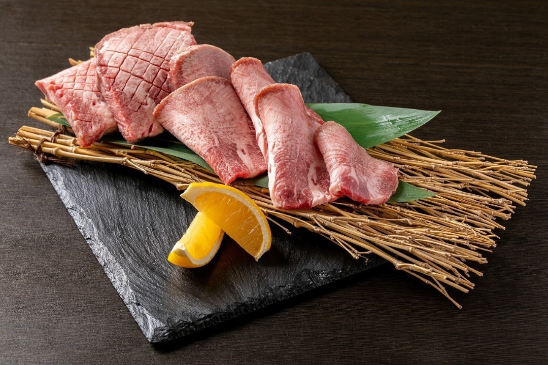 Fine cuts of marbled beef tongue presented on a dark stone plate