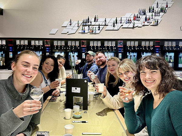Group enjoying sake tasting in modern setting with artful bottle display