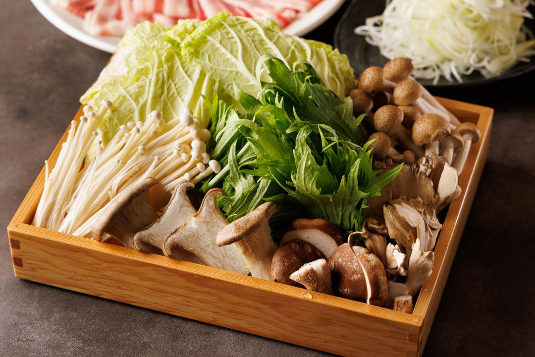 Assorted fresh mushrooms and greens in a wooden box for a gourmet meal