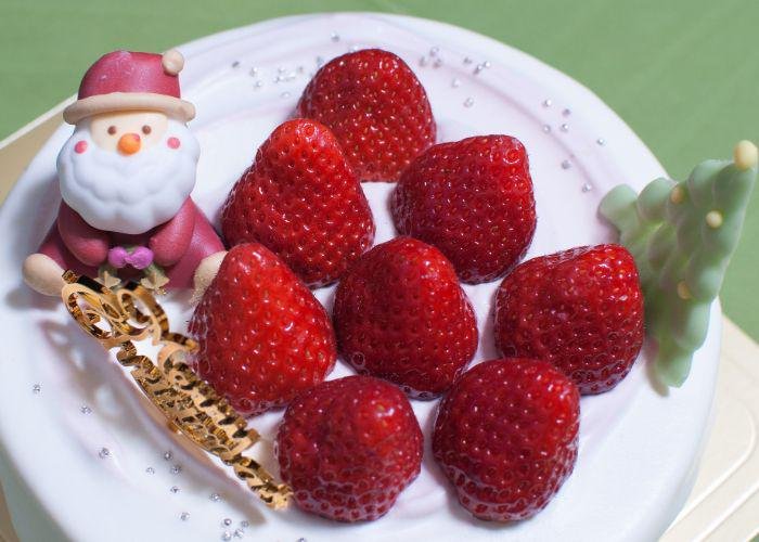 A Japanese Christmas cake that is covered in white icing with strawberry mountains and a small santa and christmas tree decorations on top