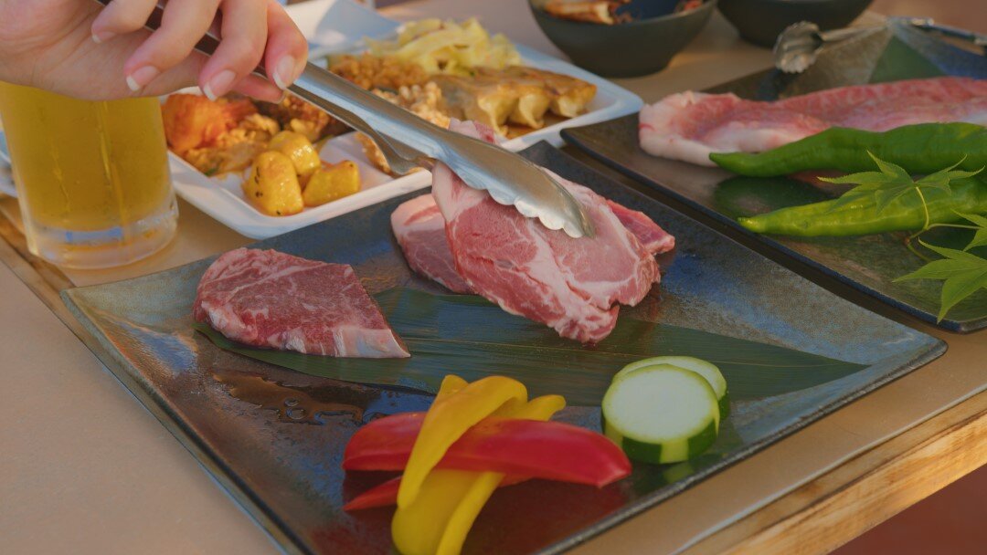 Grilled meat and vegetables on black plates with person using tongs