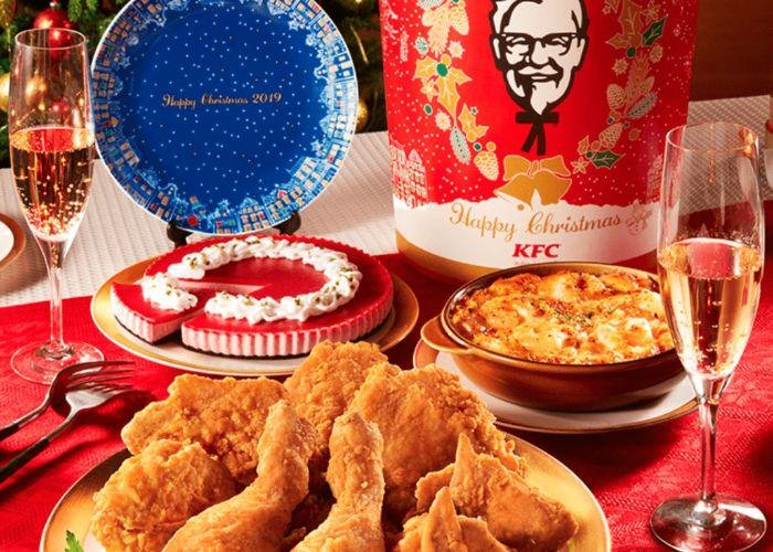 A KFC Christmas spread on a red table cloth with fried chicken, a chicken bucket and champagne flutes