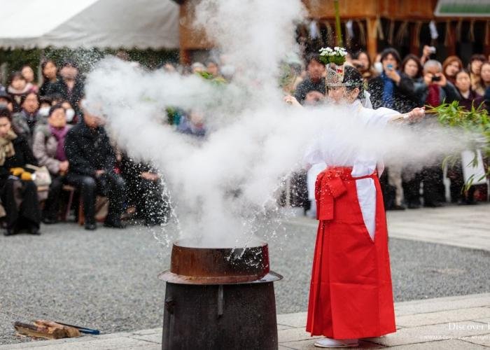 A shrine maiden is splashing the boiling sacred water with a leafy bamboo stick