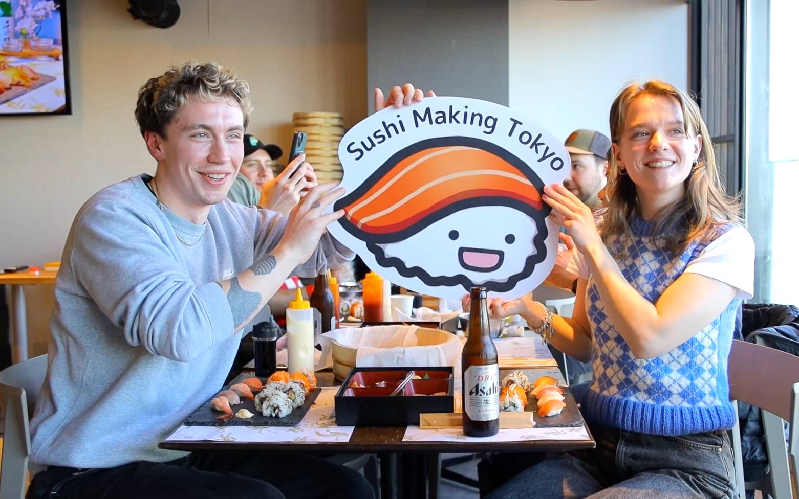 Smiling duo holding Sushi Making Tokyo sign at a restaurant