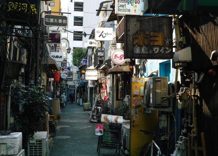 An alleyway in Shinjuku with lots of signs hanging on the sides of buildings