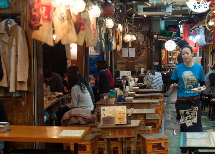 An undercover yokocho with people sitting on tables and chairs outside