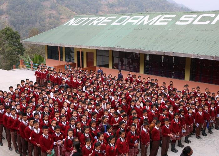 Students wearing red sweaters stand outside Notre Dame School in Kainjalia 
