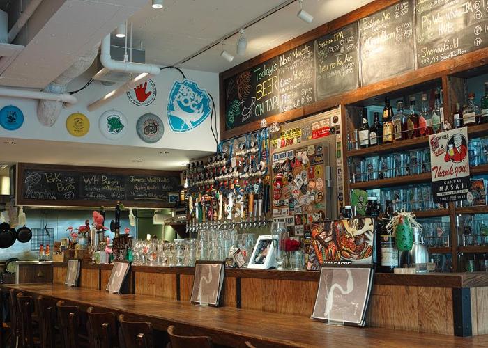 Bar counter with taps, glasses and menu written on blackboard.