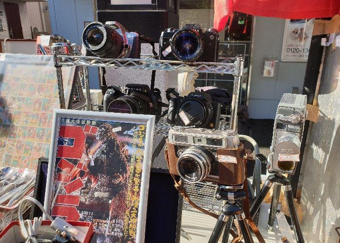 Several film cameras and a vintage Godzilla poster ona second stall