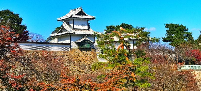 The historic white Kanazawa Castle, surrounded by the reds and oranges of fall foliage.