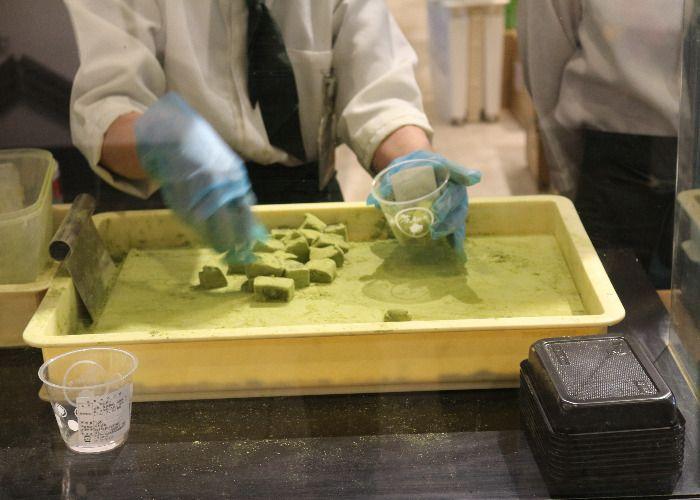 The shop clerk is filling a plastic cup with fresh matcha-powdered jellies