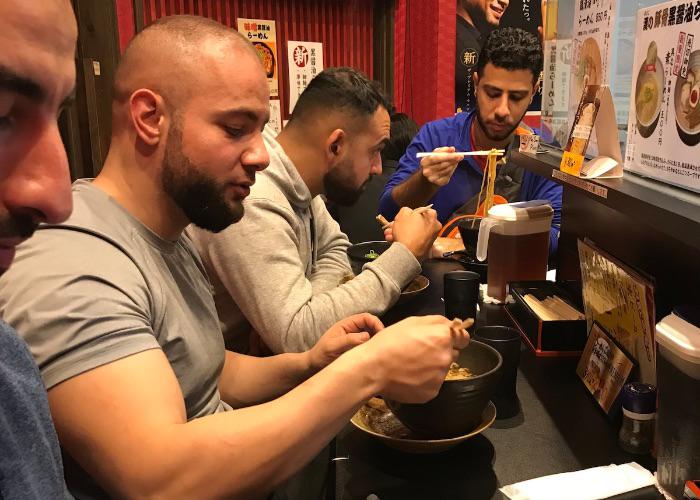 Guests of a food and drink tour of Osaka at night, enjoying ramen.