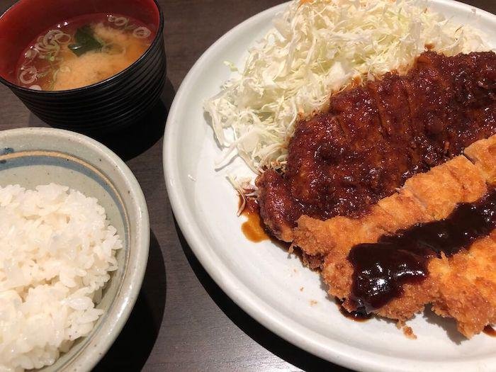Nagoya-style red miso dish, a miso katsu set meal with a crispy golden brown cut of deep-fried pork drizzled in miso glaze, served with cabbage, rice, and miso soup