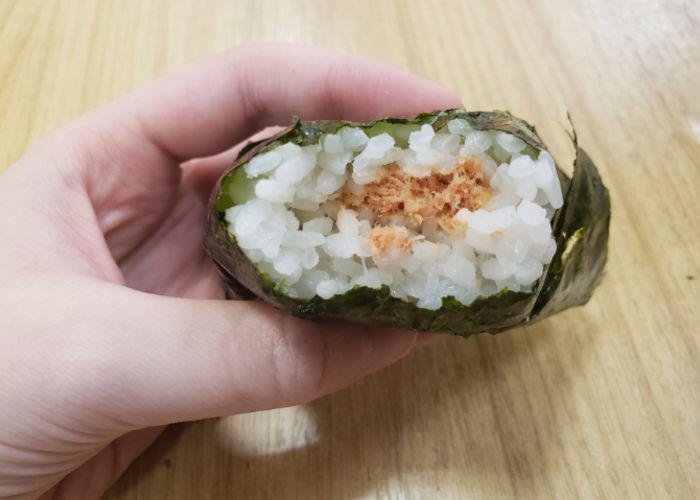 Hand holds out an onigiri with a bite taken out of it, revealing the center of grilled salmon