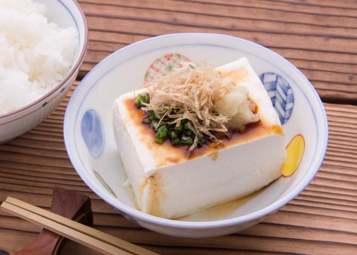 Cold Japanese tofu drizzled in soy sauce next to a bowl of rice