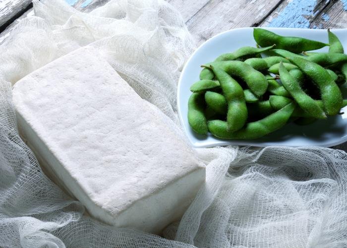 Block of firm Japanese tofu next to a bowl of edamame soybeans
