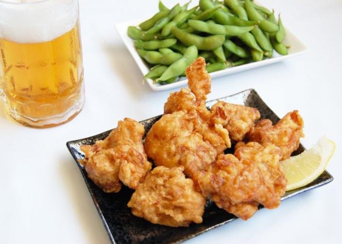 Japanese fried chicken, karaage, on a plate with a slice of lemon and a plate of edamame in the background
