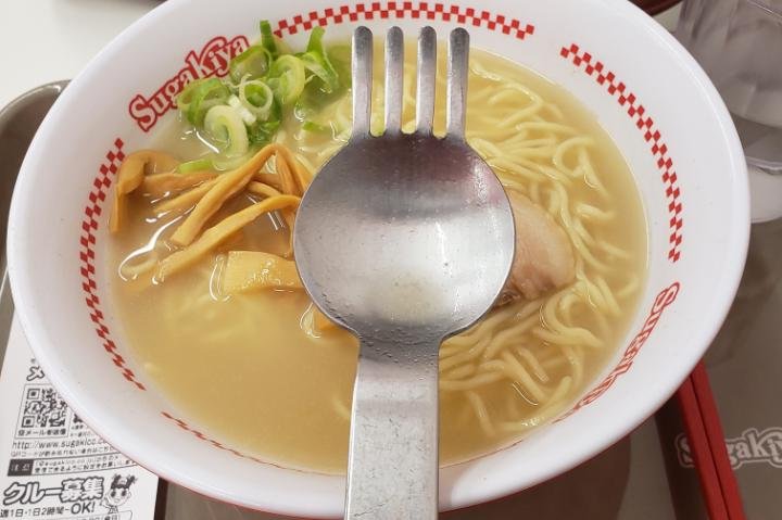 Spork with large spoon part below tines above bowl of ramen