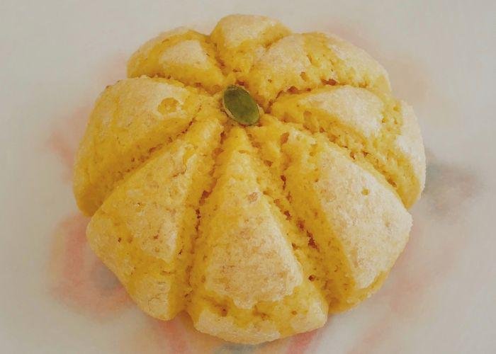 A pumpkin shaped melon pan is set on top of parchment paper. At the very top of the bread there is a pumpkin seed. 