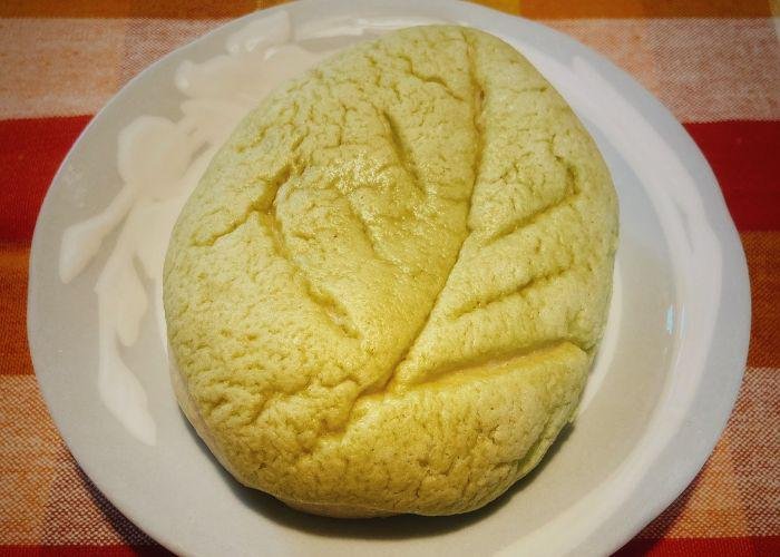 The melon flavor melon pan is set on top of a plate. The bread does not have the typical crisscrossed shape. Instead, it resembles a leaf.