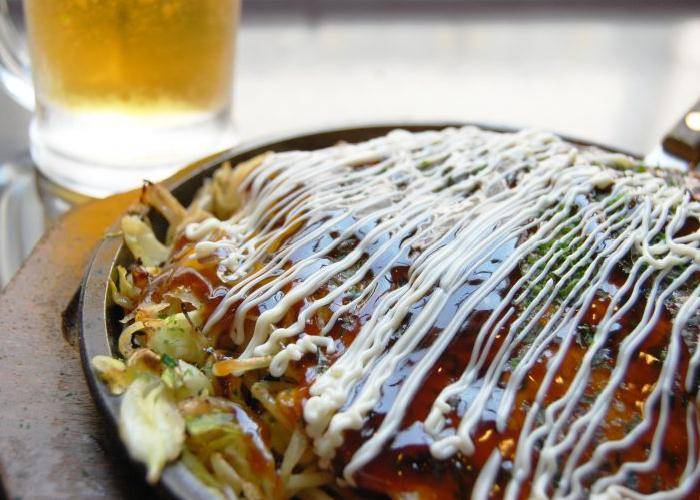Okinomiyaki topped with sauce, on a griddle pan.