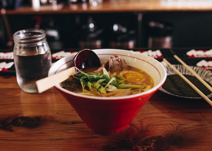 A bowl of miso ramen on a countertop, with a wooden ladle spoon resting atop.