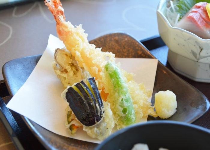 A small dish with a lightly-colored piece of prawn tempura, and several vegetable pieces.