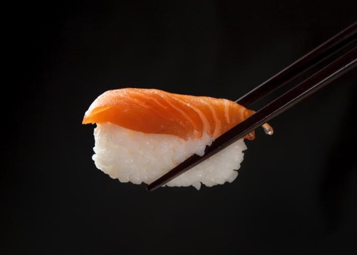 A piece of salmon nigiri sushi on a black backdrop