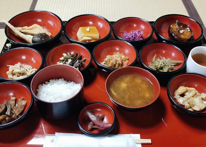 Shojin Ryori, the traditional Japanese vegetarian and Buddhist cuisine. A red tray with a variety of small matching red bowls holding various Japanese vegetarian foods like goma dofu and vegetables