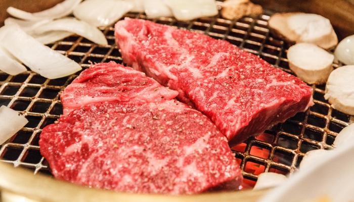 Two thick cuts of wagyu beef grilling, sprinkled with seasoning.