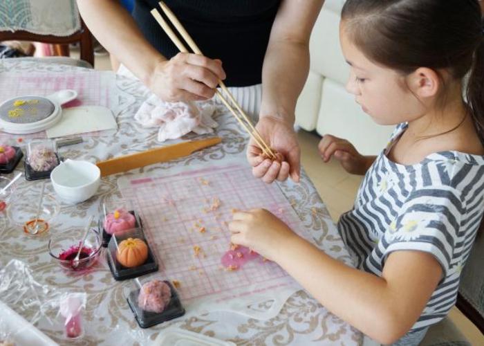 adult helping child make wagashi with chopsticks, colorful flower-shaped wagashi on table