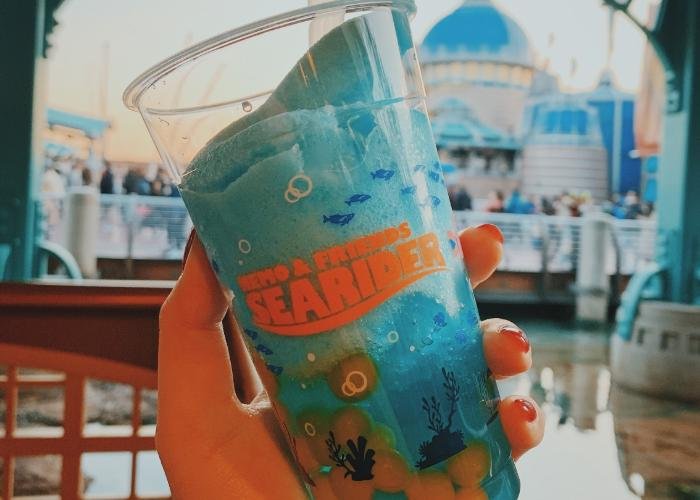 The Deep Sea Pineapple Smoothie has orange boba balls on the bottom. The cup is clear and shows the blue slushy. The cup is decorated with coral and reef sillohetes towards the bottom and a Nemo and Friends Searider logo is on the middle of the cup. 
