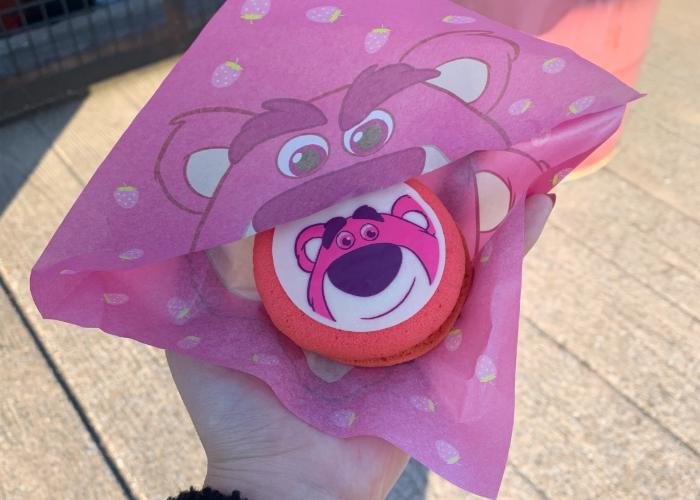 A bright pink cookie sandwich is being held. A picture of Lotso from Toy Story is displayed on top of the cookie. Around the Cookie is a wrapper with Lotso's face. 