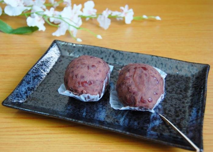 Bota Mochi, also known as Ohagi, on a black plate. A piece of mochi coated in red bean paste.