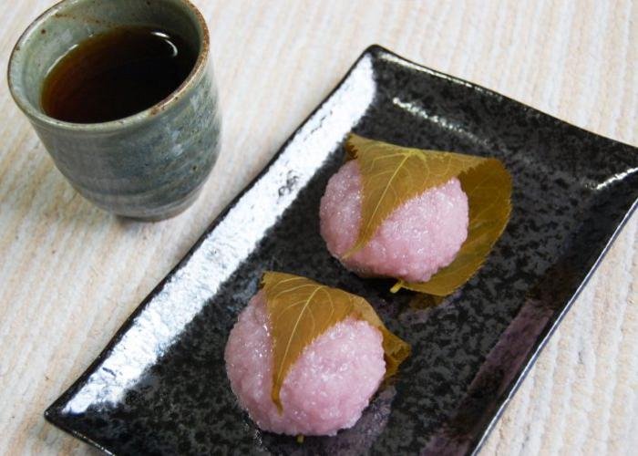 Pink sakura mochi on a plate with a cup of tea