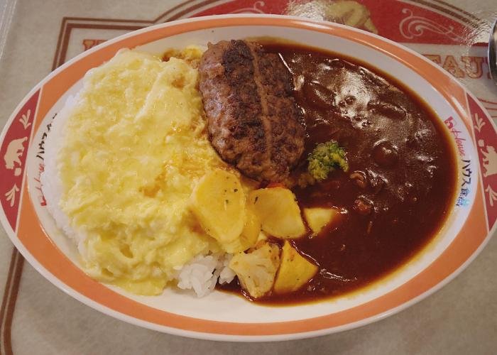 A large plate filled is filled with curry on the right and rice and eggs on the left. In the middle is sliced up rounds of potato and a meat patty. 