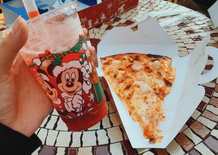 On the left of the picure is Mickey's Sparkling Boba. On the right is the seafood pizza, topped with cheese, scallop, and shrimp. It is placed on a white, triangle shaped paper platter.