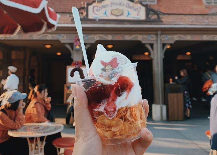 A cup filled with cereal, soft serve, and raspberry cream is displayed. The soft serve is twirled all the way to the top and a biscuit with Captain Hook's face is placed on it. In the background is Captain Hook's Gallery.
