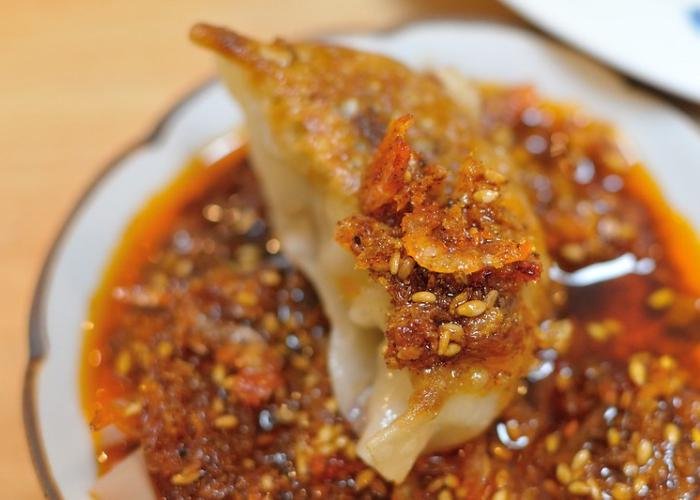 Gyoza potsticker dipped in brown-red chili oil in white dish